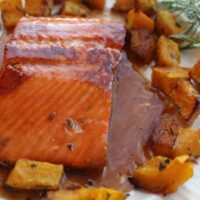 Glazed salmon fillet inspired by the Sweet Bourbon Salmon Recipe, served with roasted diced butternut squash and a sprig of rosemary on a plate.