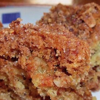 Close-up of a crumbly, golden-brown Sour Cream Cinnamon Crumb Coffee Cake slice with a crunchy streusel topping, showing a moist, textured interior on a white plate.