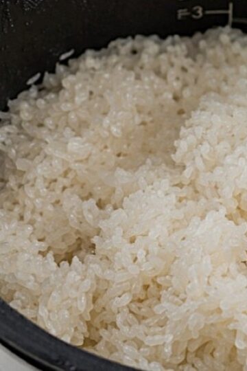 Close-up of freshly cooked sticky rice inside a rice cooker, showing fluffy and slightly sticky grains with measurement markings visible on the inside of the pot.