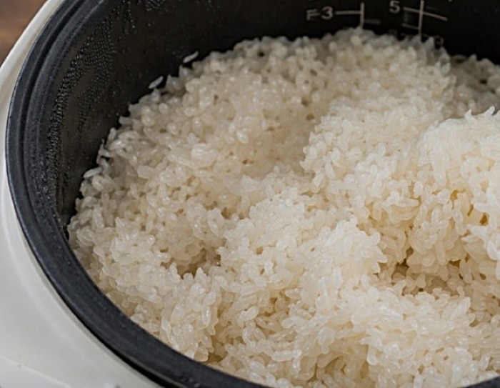Close-up of freshly cooked sticky rice inside a rice cooker, showing fluffy and slightly sticky grains with measurement markings visible on the inside of the pot.