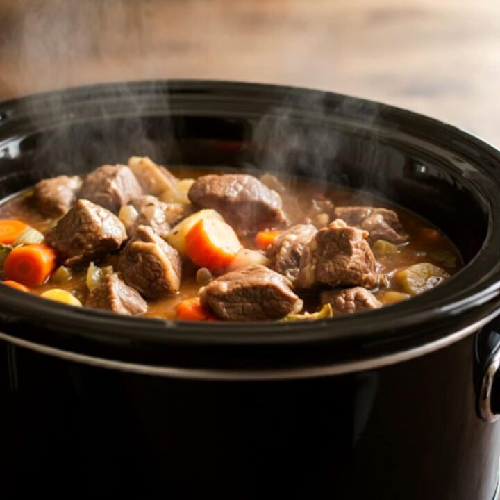 A black slow cooker filled with steaming Instant Pot Lamb Stew, featuring tender lamb, carrots, potatoes, and other vegetables simmered in a rich, flavorful broth.