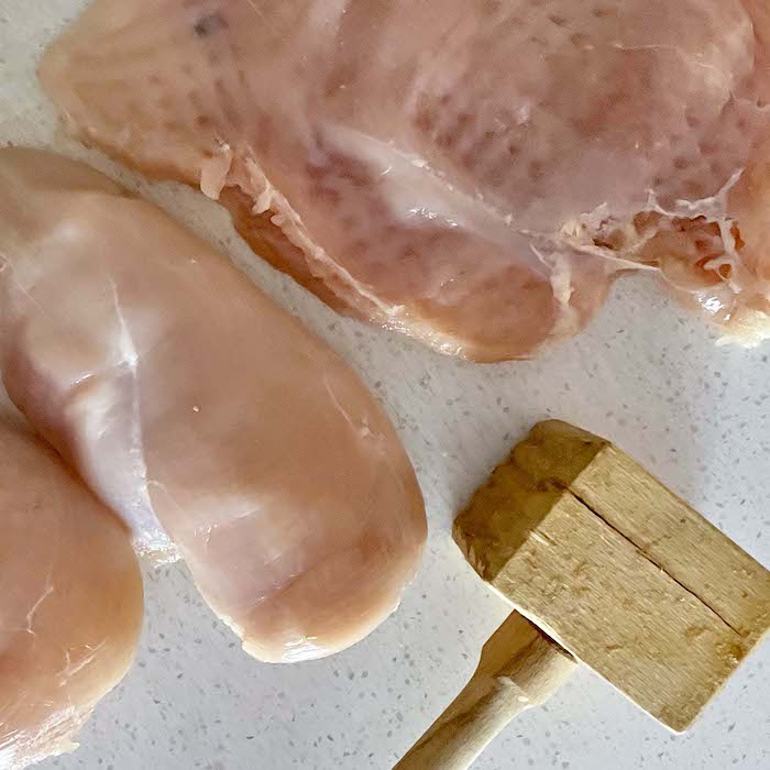 Pound the raw chicken with a mallet to tenderize.