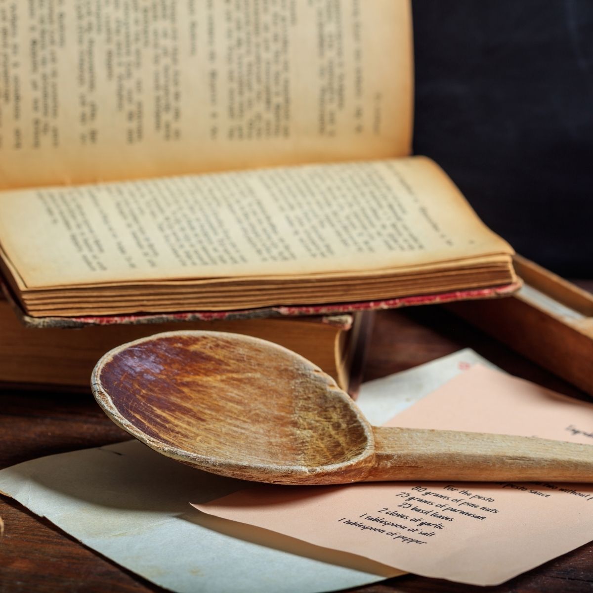 an old open cookbook next to a wooden spoon