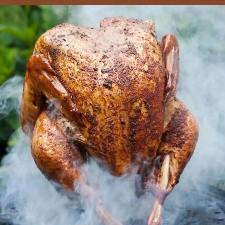 A whole, seasoned turkey in a propane smoker is being smoked outdoors. Thick, white smoke surrounds the golden-brown bird, highlighting its crispy skin against a backdrop of blurred greenery.
