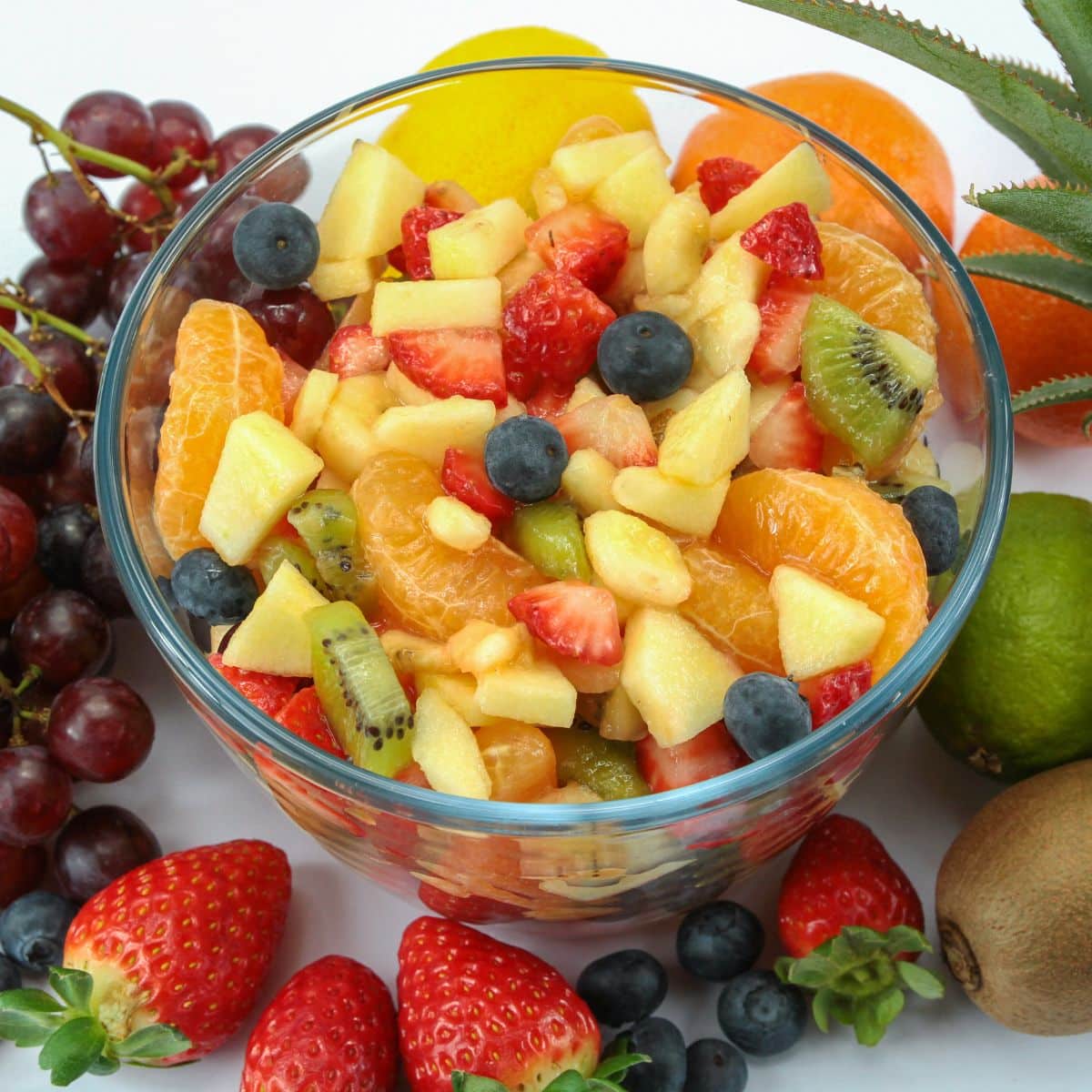 colorful fruit salad in a glass bowl, surrounded by fresh fruits.