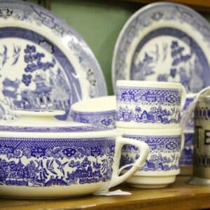 A blue willow dish set sitting on a wooden shelf.