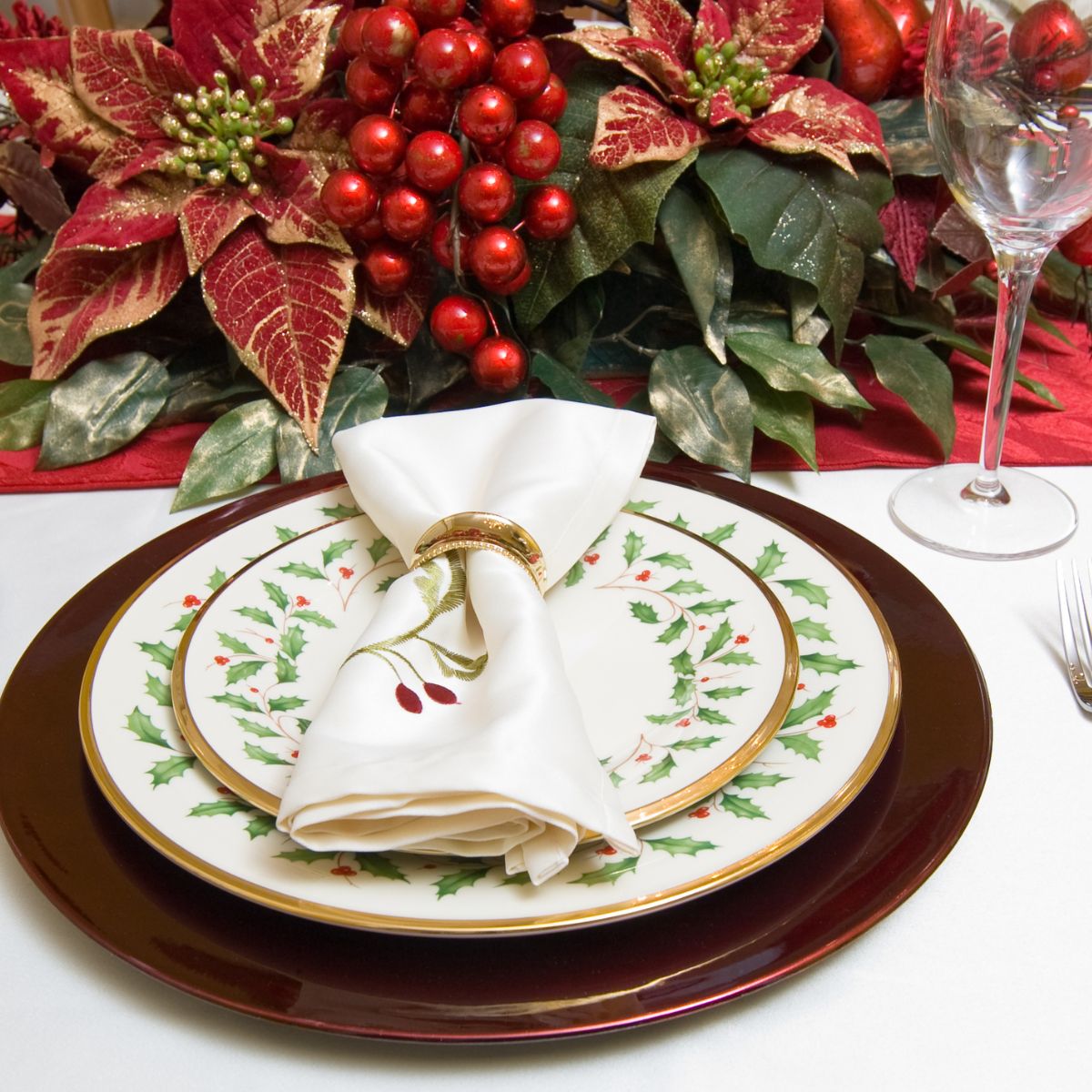 Christmas plates set up for dinner with poinsettia in the background.