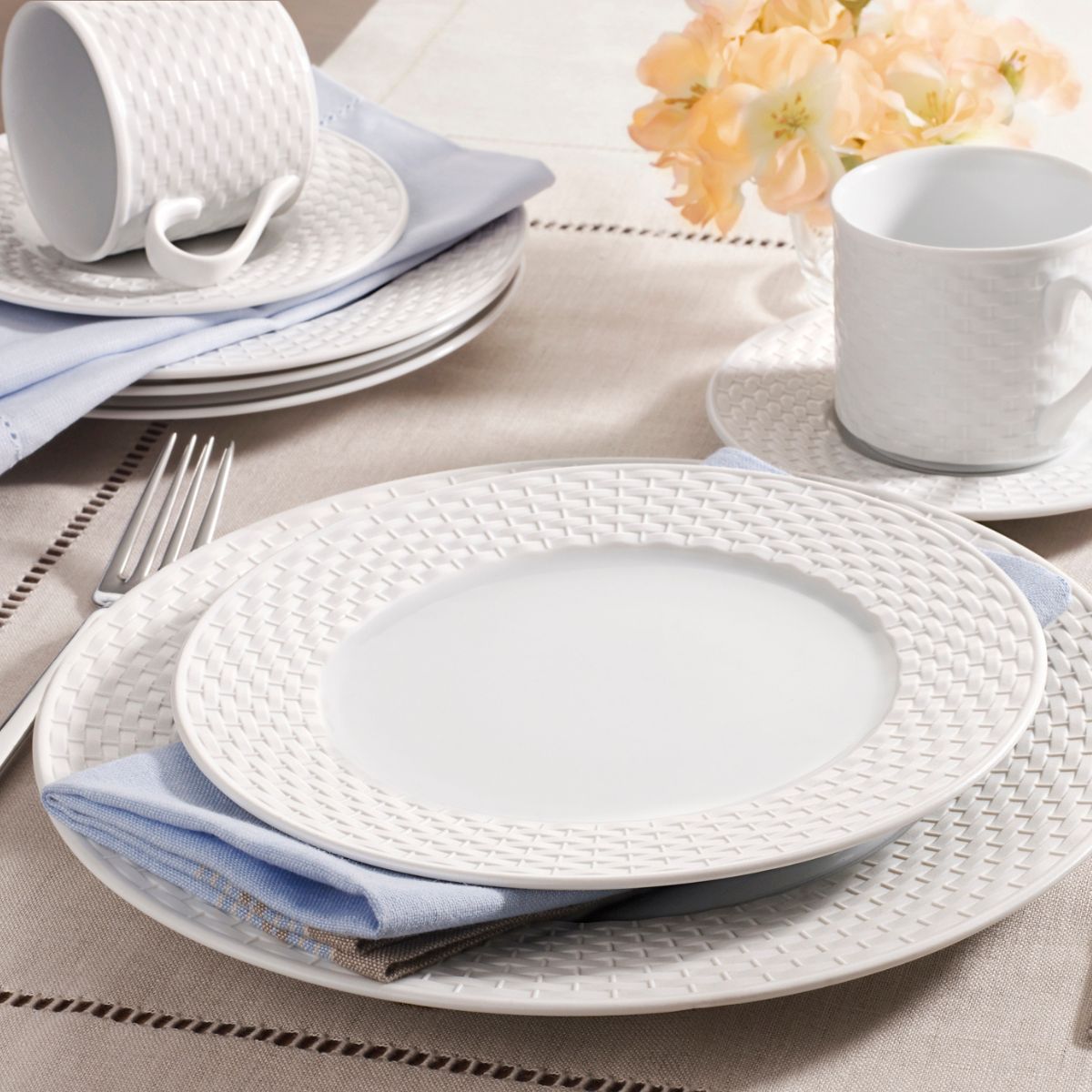 White dinnerware with a basket weave design set up on a table with blue cloth napkins.