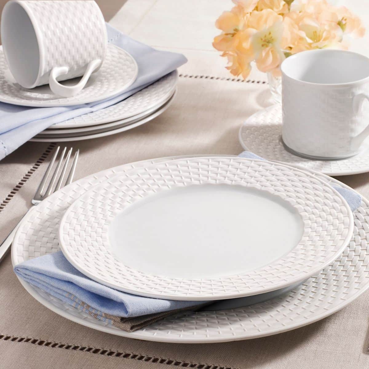 White plates with a basket weave design set on a table with light blue cloth napkins.