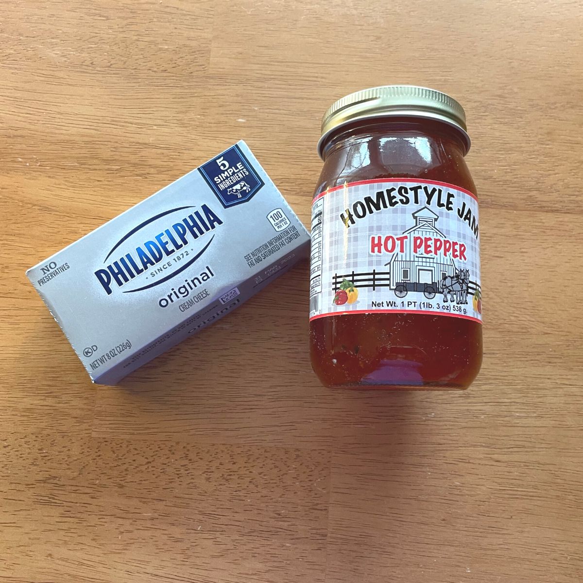 A jar of hot pepper jelly and a packet of cream cheese sitting on a wooden table.