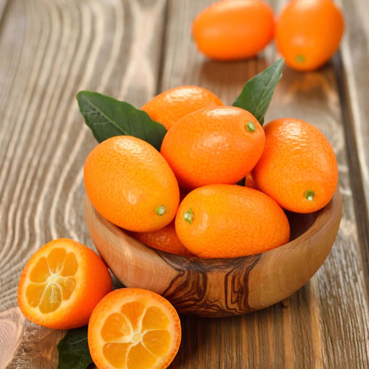 a bowl of kumquat fruits on a wooden table. 