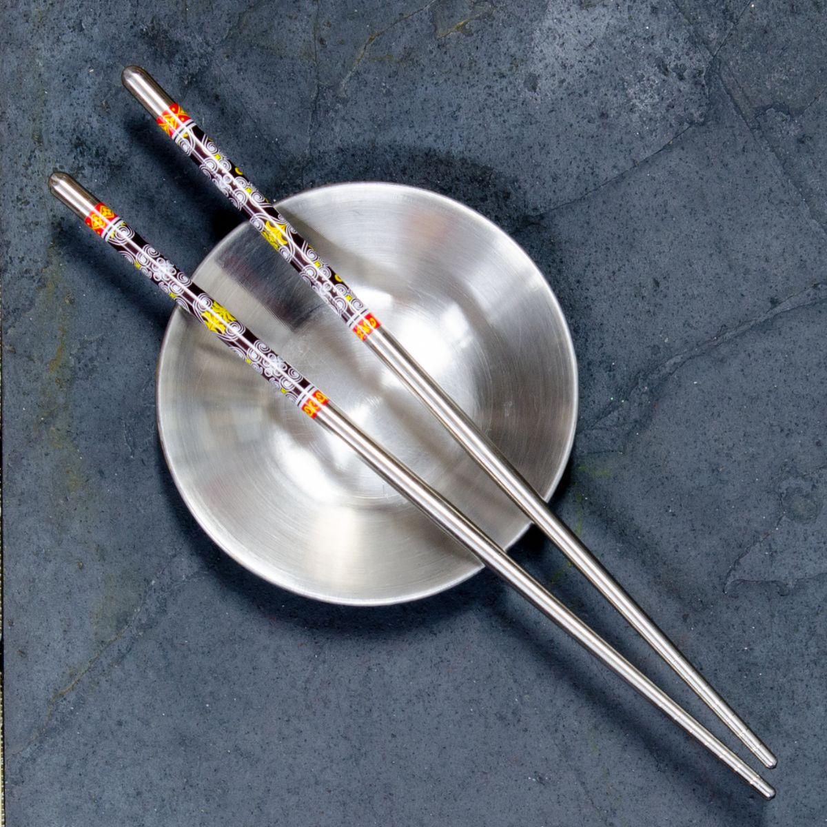 a steainless steel bowl with chopsticks laying on top.