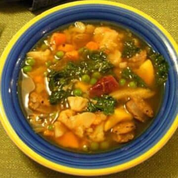 A beautiful blue and yellow bowl filled with vegetable soup.