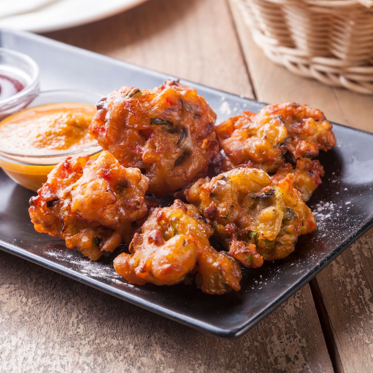 Rice pakoras and sauce on a black plate.