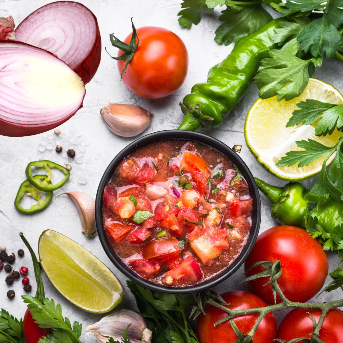 A bowl of salsa surrounded by fresh vegetables.