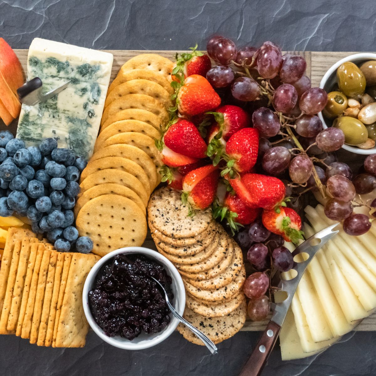 a wooden cutting board piled with cheeses, crackers and fruits.