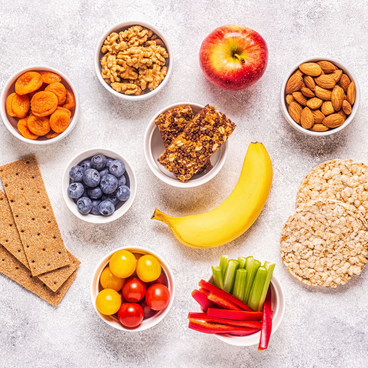 a display of healthy snacks: nuts, almonds, dried fruit, fresh fruits and vegetables, and crackers.