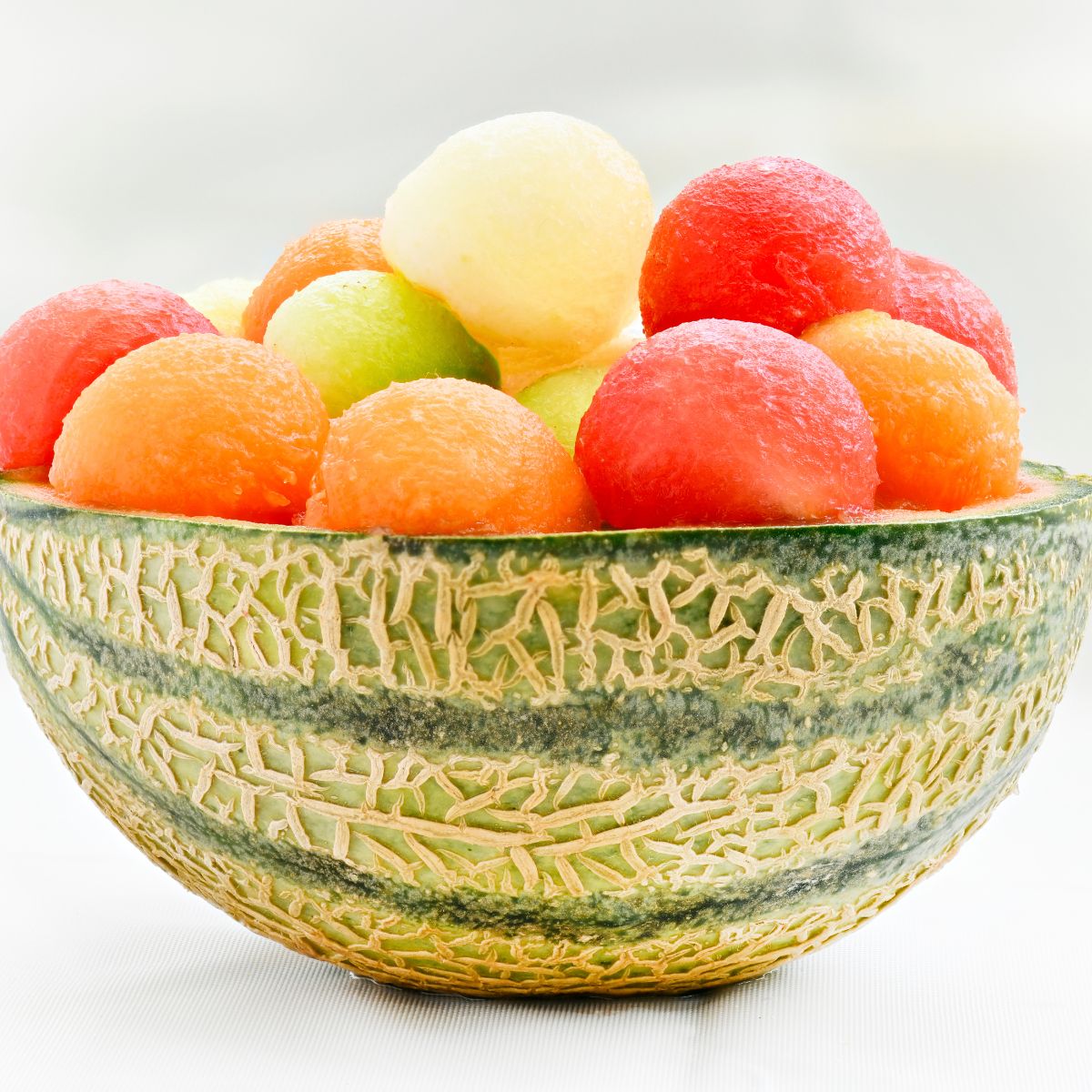 colorful melon balls arranged in a bowl made out of the melon rind. 