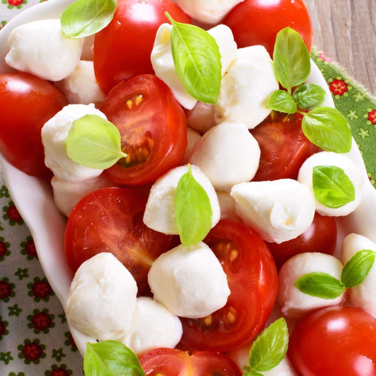 sliced tomatoes with mozzarella balls and basil nestles in a white porcelain dish.