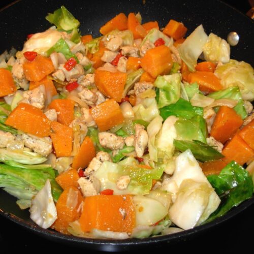 a bowl of colorful stir-fry made with cabbage, sweet potatoes, and chicken.