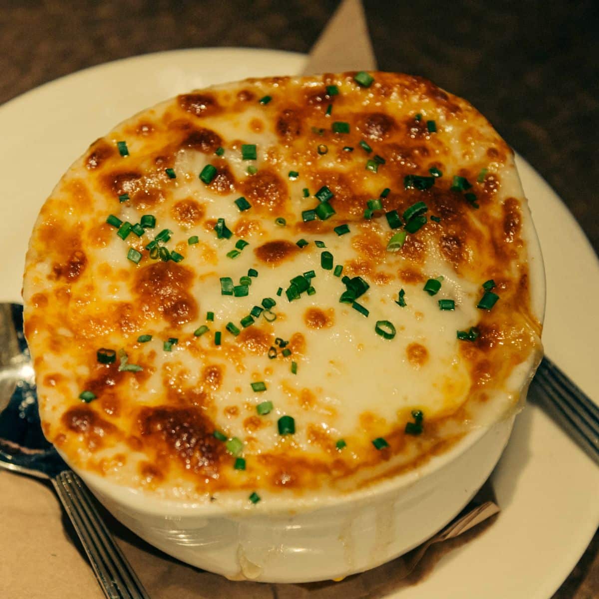 a bowl of crusty French onion soup on a plate. 