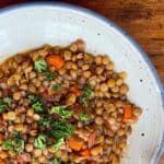 Lentil soup with colorful chunks of carrots and bright green parsley in a light blue ceramic bowl