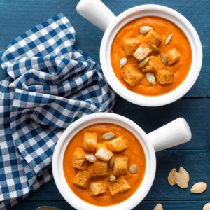 Two bowls of creamy pumpkin soup topped with crunchy croutons and pumpkin seeds.
