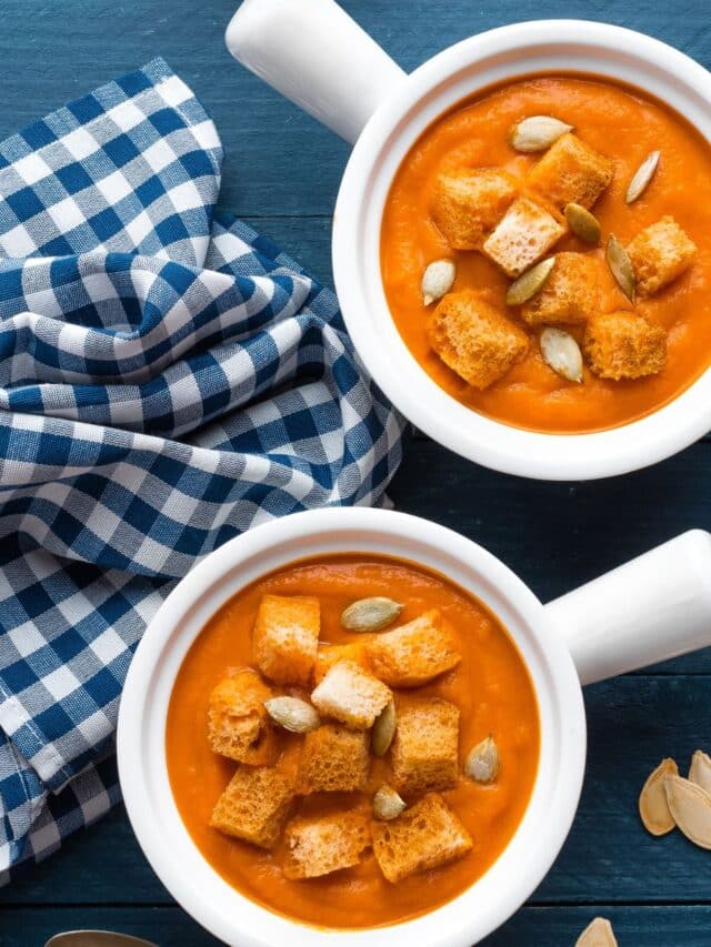 Two bowls of creamy pumpkin soup topped with crunchy croutons and pumpkin seeds.