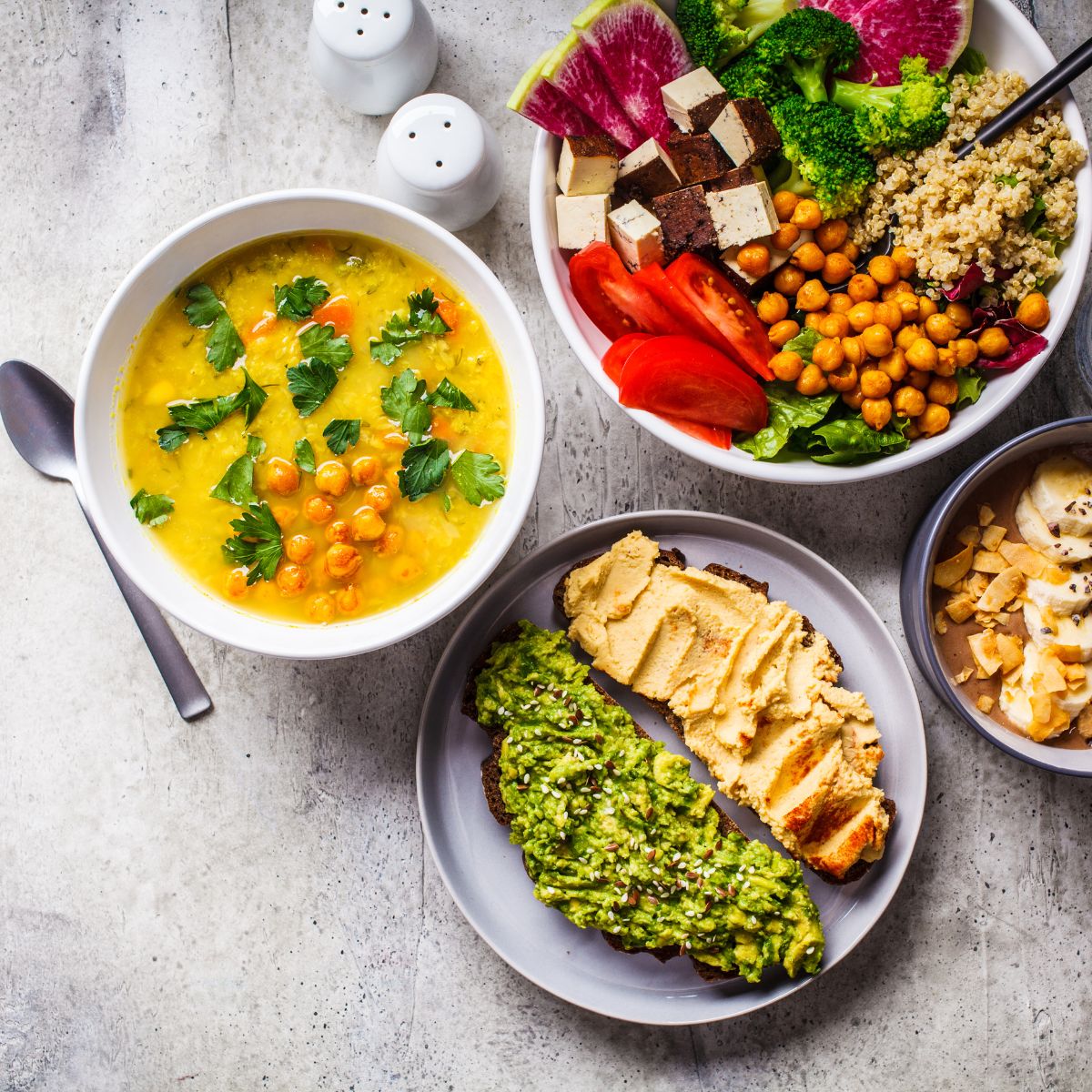 A colorful dinner meal including a bowl of soup, salad, and bread slices covered with spread. 