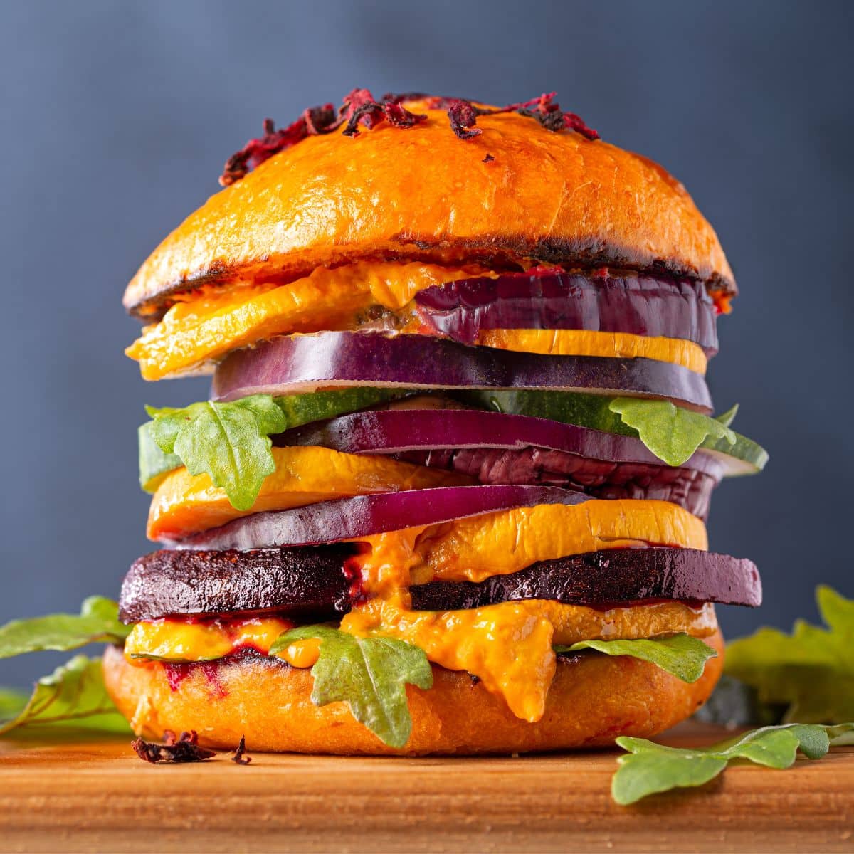 A tall sandwich with red onions, roasted beets and sweet potato, cheese and fresh lettuce.