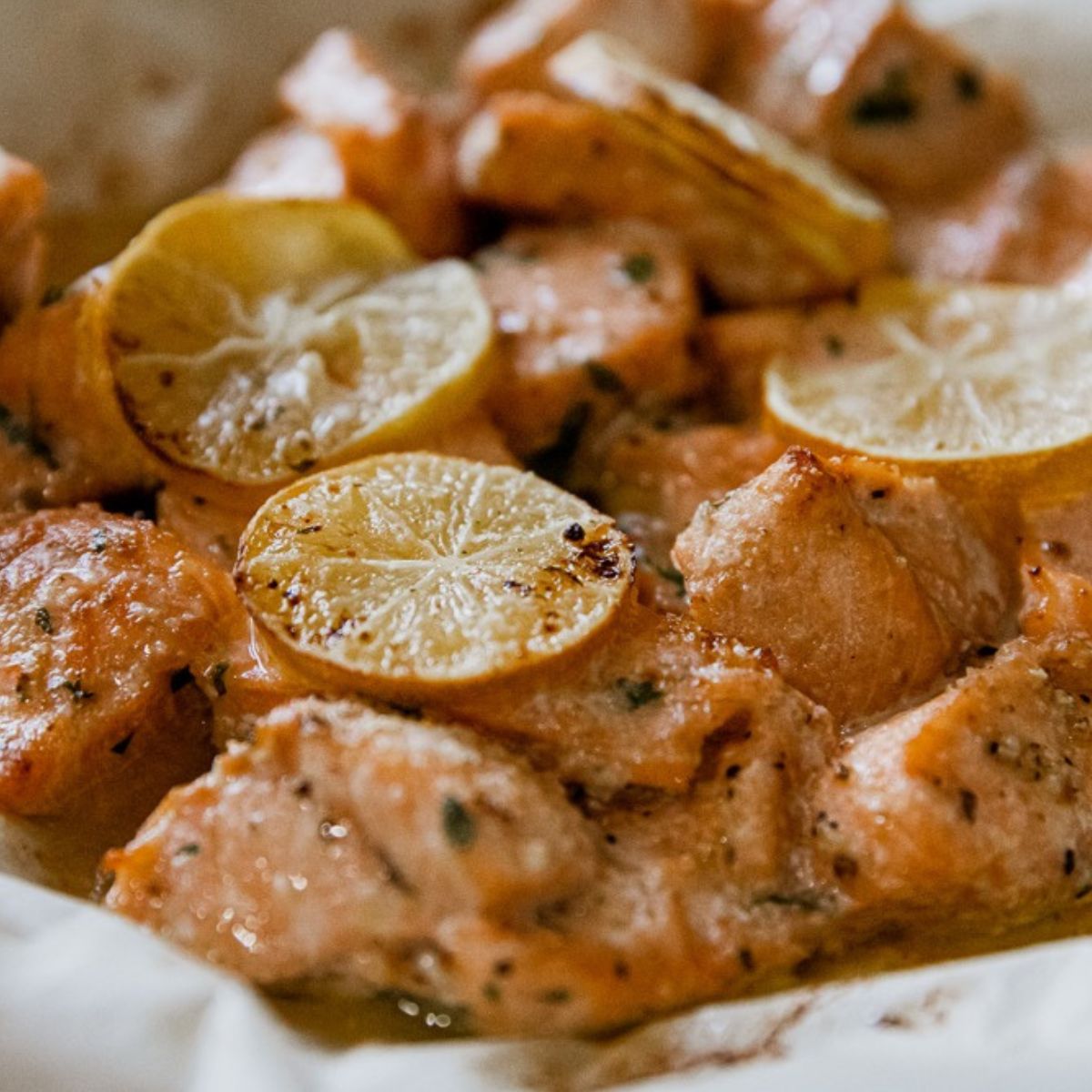 A pile of salmon bites with roasted lemons. 