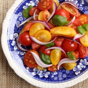 Colorful cherry tomatoes and onion salad on a pretty white and blue floral plate.
