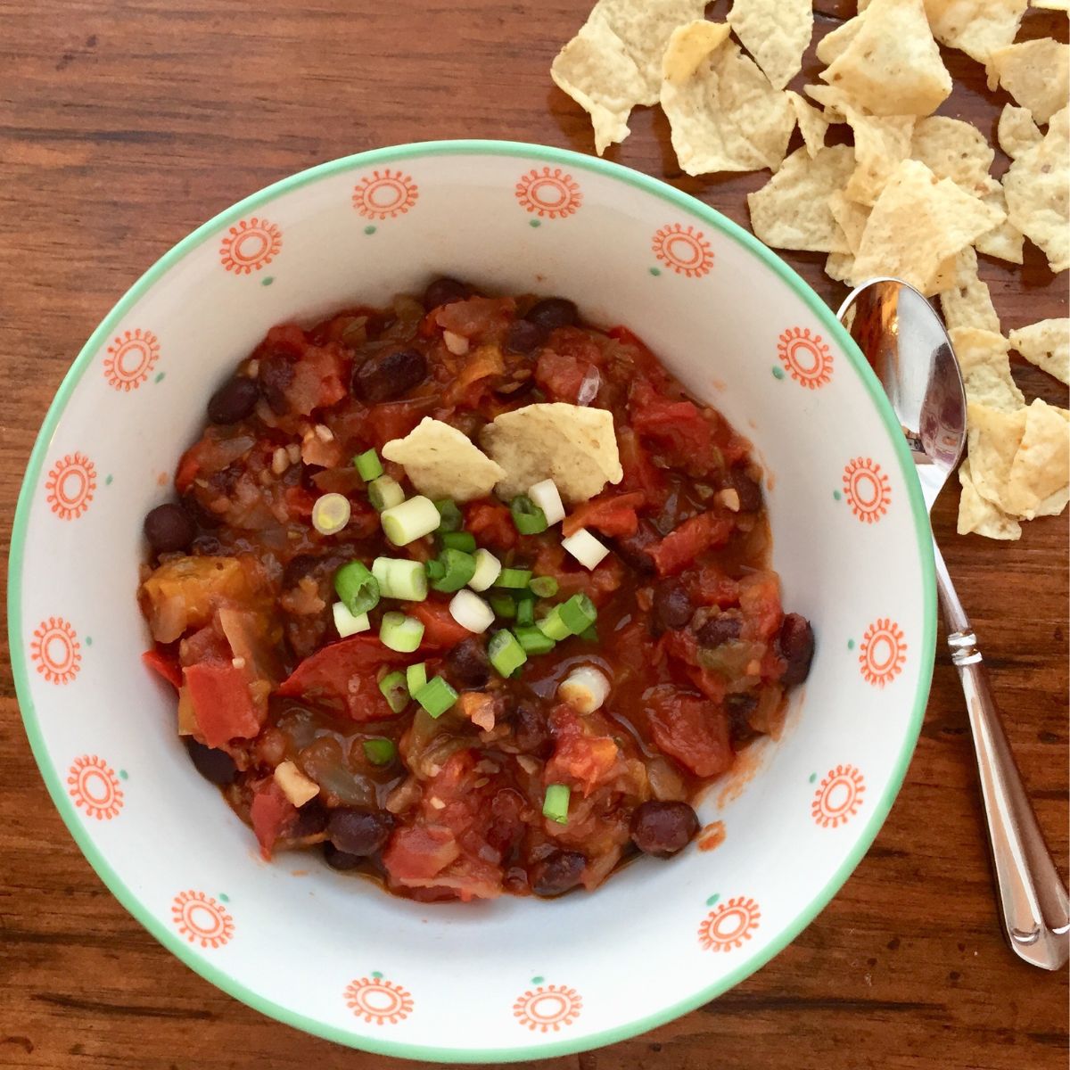 A bowl of plant based black bean chili and fritos chips.