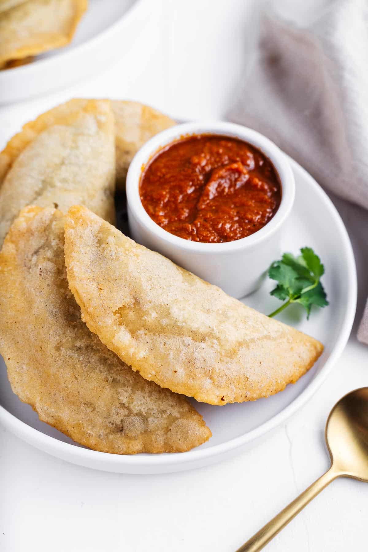 A plate of empanadas with some red sauce.