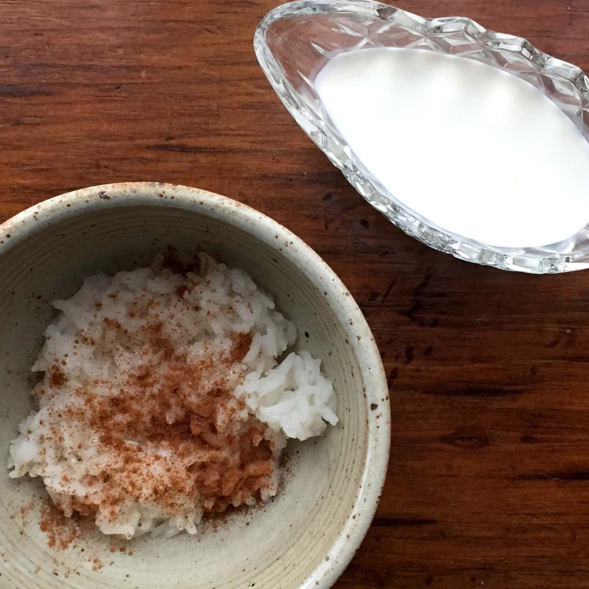 A bowl of rice with cinnamon on top and a dish of milk to pour on top of it.