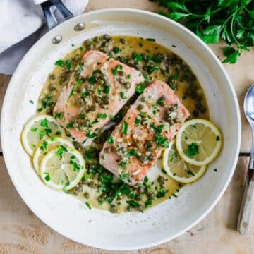 Salmon drenched in sauce with lemons on the side.