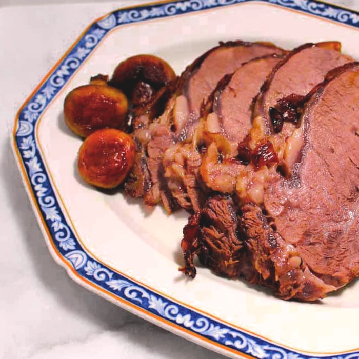 Slices of a cooked prime rib roast served with whole mushrooms on a white octagonal plate with a blue decorative rim.