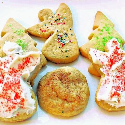 A plate of festive sugar cookies and Brown Sugar Cookies, shaped like trees and angels, decorated with colored sugar and sprinkles, alongside a round cookie with a cinnamon topping.