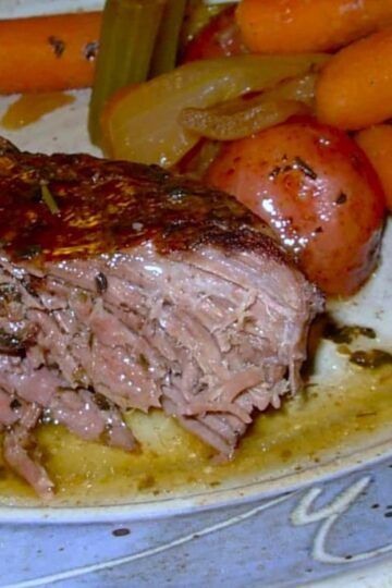 A plate with a serving of tender Winter Pot Roast, featuring baby carrots, red potatoes, celery, and onions in savory gravy—an inviting beef roast recipe perfect for chilly evenings.