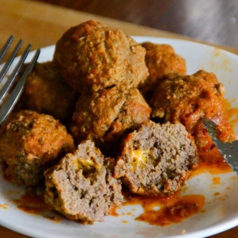A plate with several beef meatballs, one cut open to show a cheesy filling, topped with tomato sauce. A fork and knife rest on the plate, which is set on a wooden surface—perfect Instant Pot comfort food.