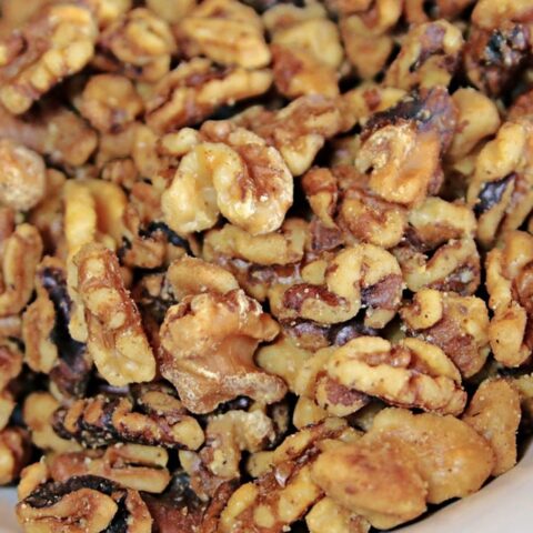 A close-up view of a bowl filled with shelled walnut halves and pieces, showcasing their rough, crinkled texture and brown, tan coloration—perfect to toast walnuts for extra depth of flavor.