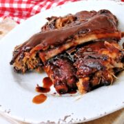 Instant Pot Dump and Go Country Style Ribs coated in a glossy, dark sauce are served on a white plate, with a red and white checkered cloth in the background.