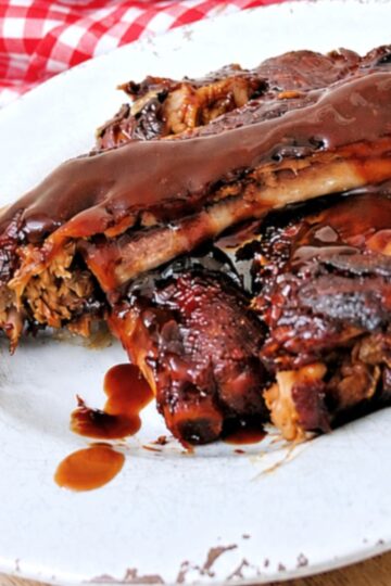 Instant Pot Dump and Go Country Style Ribs coated in a glossy, dark sauce are served on a white plate, with a red and white checkered cloth in the background.