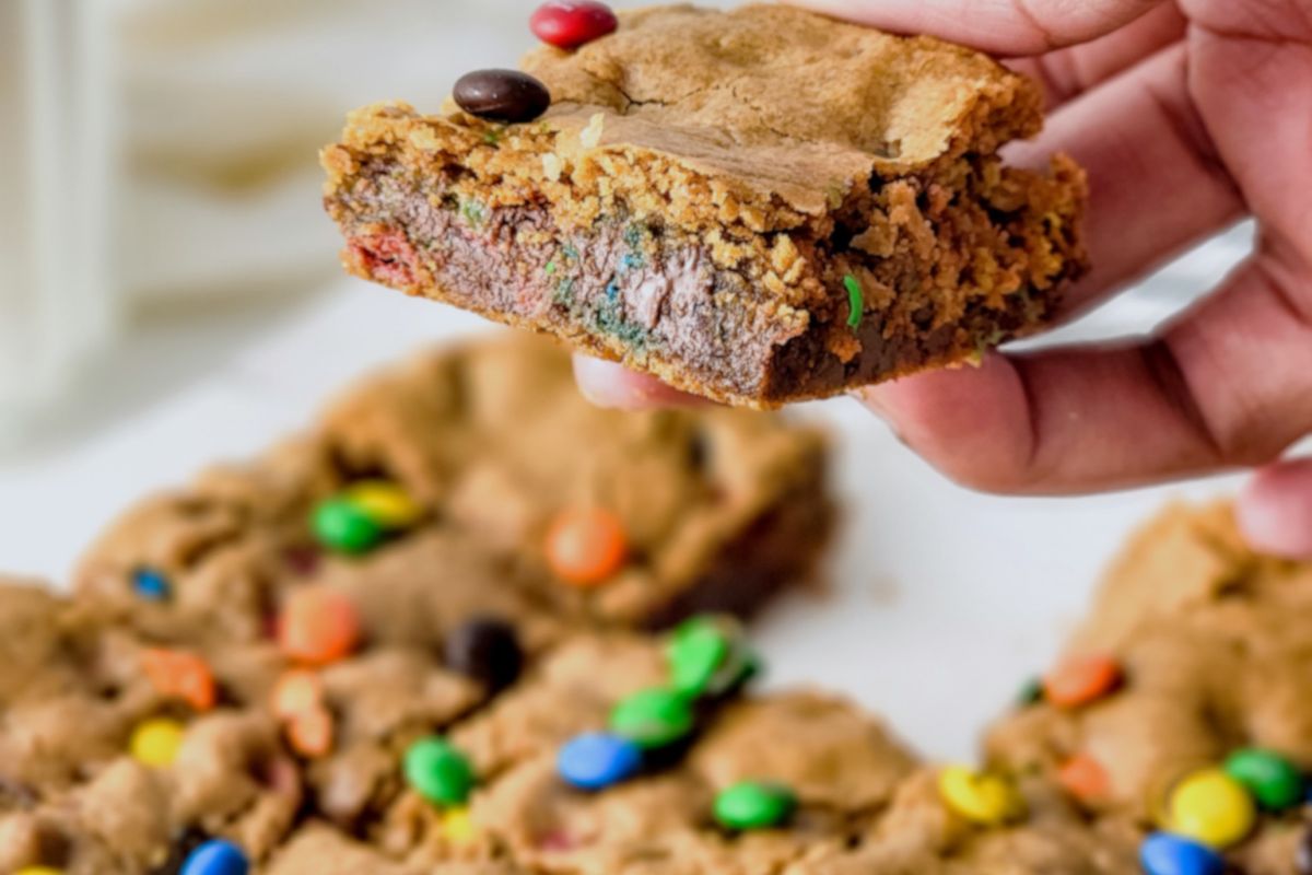 Close-up of chewy M&M cookie bars cut into squares, showing golden edges and colorful candy pieces on top, served as party food.