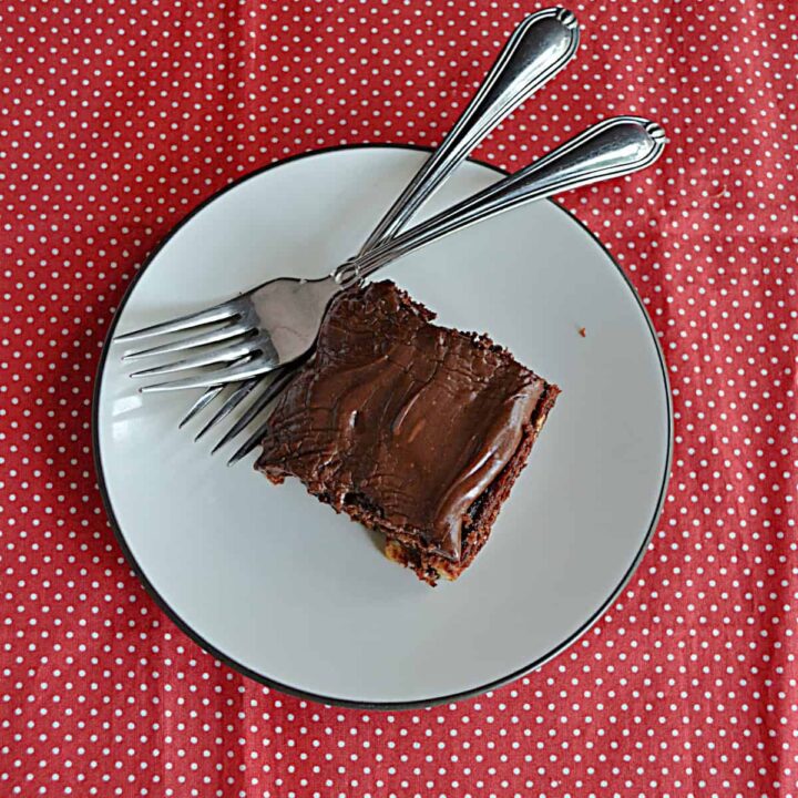 A square piece of chocolate frosted cake on a white plate with two forks, perfect for potluck desserts, sits on a red tablecloth with white polka dots.