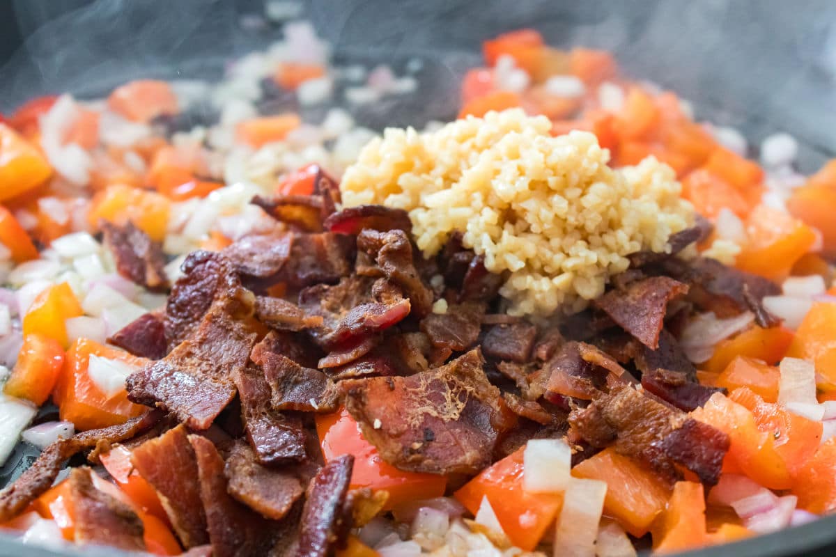adding bacon and garlic to onions and peppers