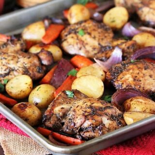A baking sheet filled with roasted chicken thighs, baby potatoes, sliced carrots, and red onion pieces, all seasoned with herbs and garnished with fresh parsley—perfect for easy one dish dinners.