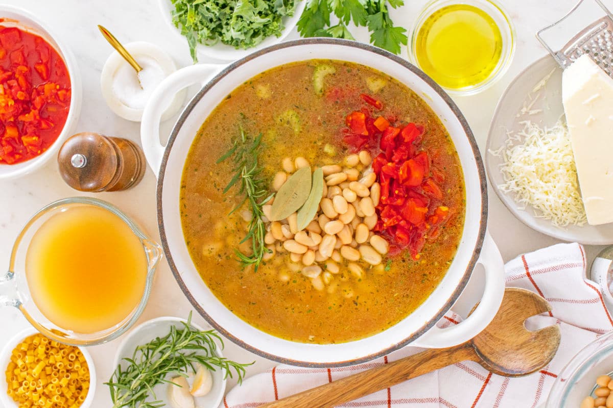 Adding broth, diced tomatoes, beans, bay leaf, and rosemary for winter minestrone.