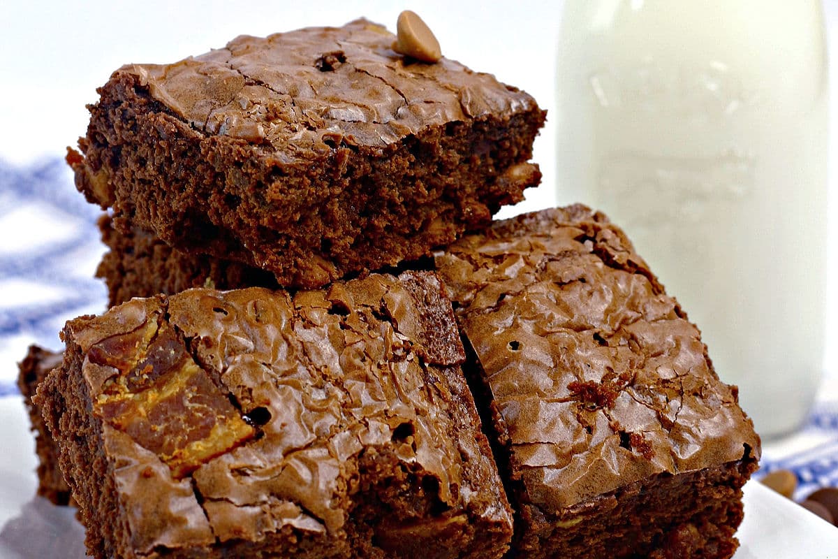 A close-up of Elvis brownies containing bananas and bacon, stacked on a plate, with a glass bottle of milk in the background. The brownies have a shiny, crackly top.