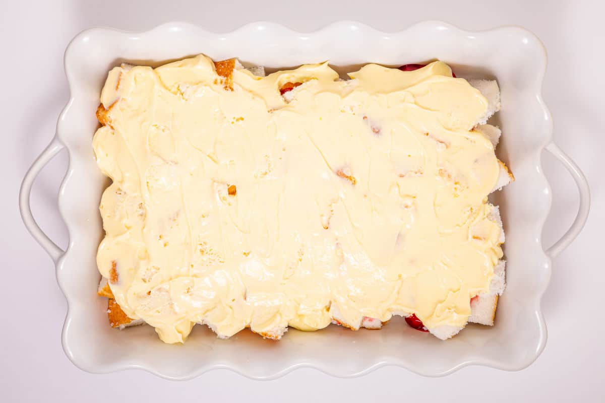 A white rectangular baking dish filled with cubed bread covered in a thick layer of creamy yellow custard, ready to be baked.